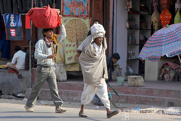 Men Walking In Street Carrying Items On Their Heads