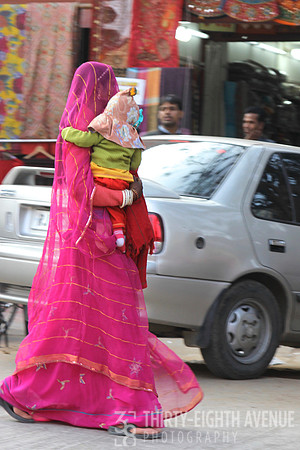 Mother In Bright Pink Sari Carrying Child Across The Street