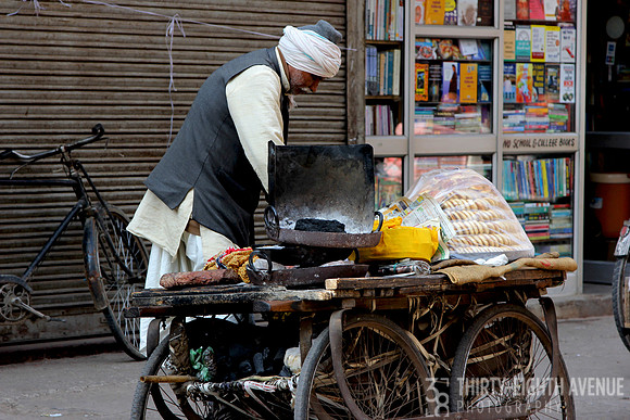 Man In Gray Vest & White Turban Cooking On Food Cart